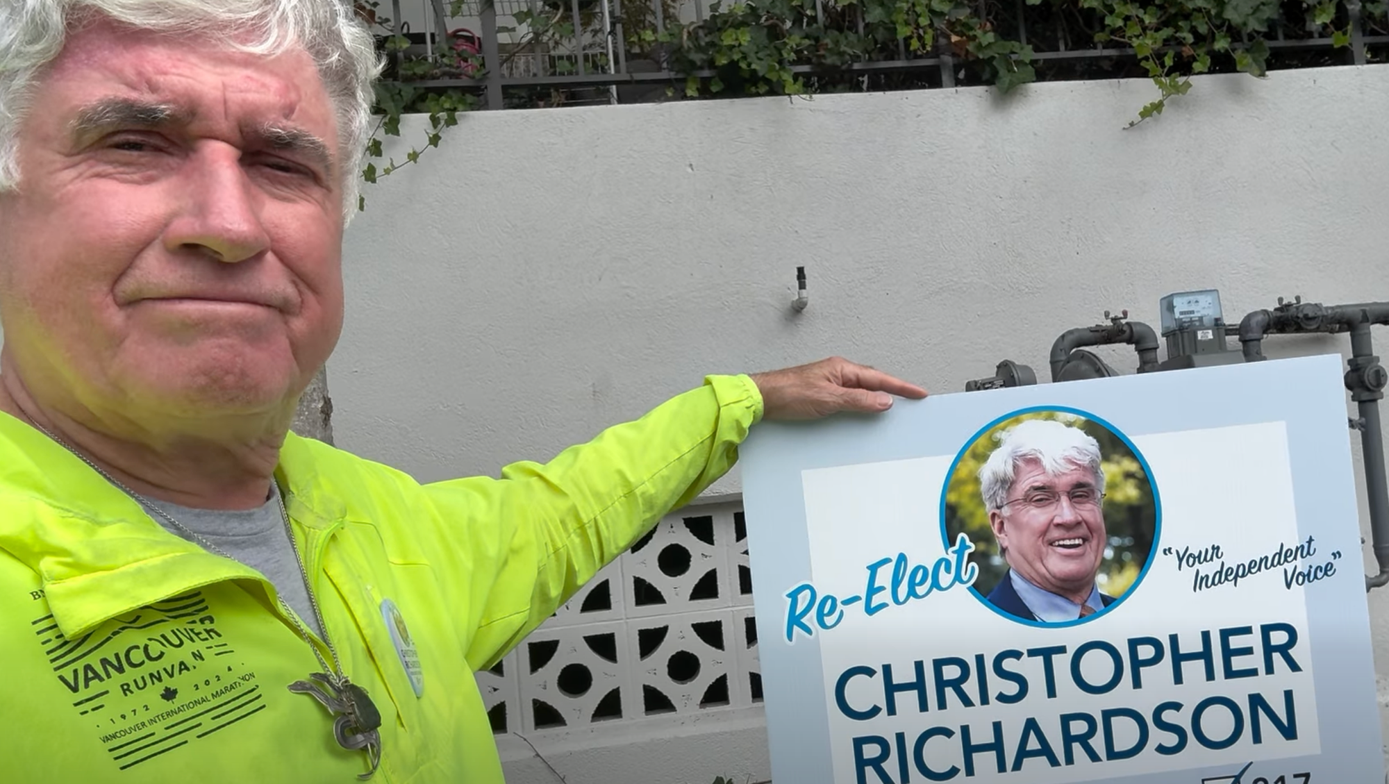 Christopher Richardson holds a sign saying Re-Elect Christopher Richardson: Your Independent Voice