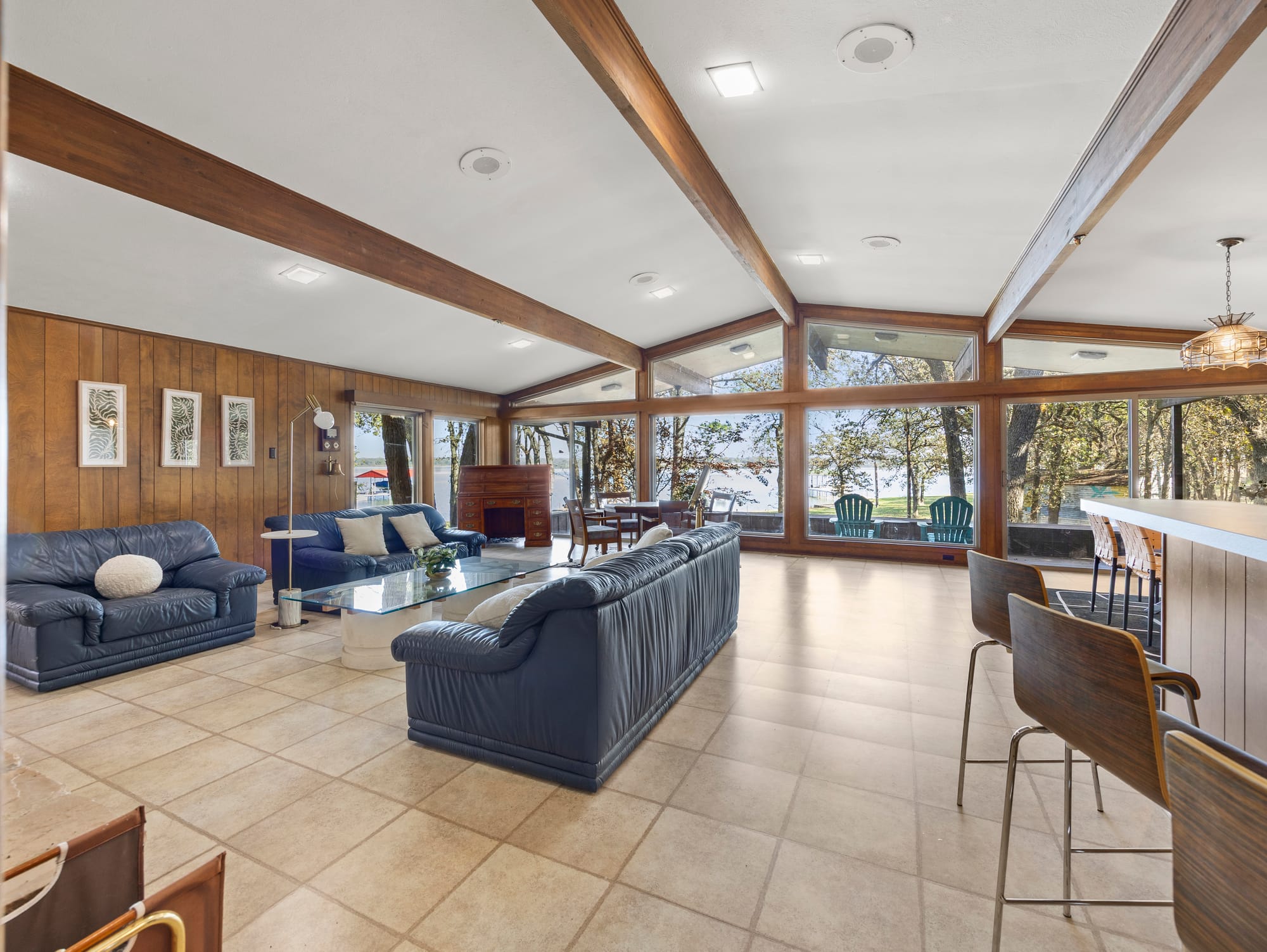 Interior of a midcentury modern living room with a stone fireplace, vaulted wood ceilings, and large windows looking out toward Eagle Mountain Lake.