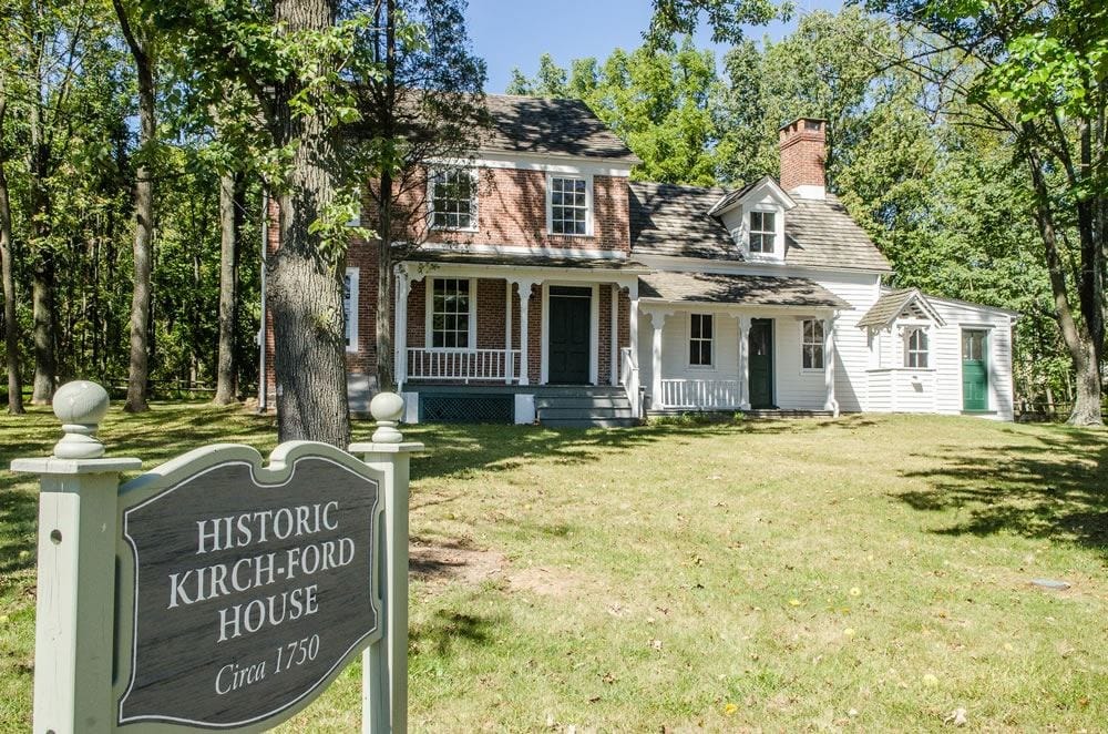 The Historic Kirch-Ford House in Warren Township, a brick two story house with a white porch joined to a white clapboard wing, a sign on the lawn reading Historic Kirch-Ford House, Circa 1750.