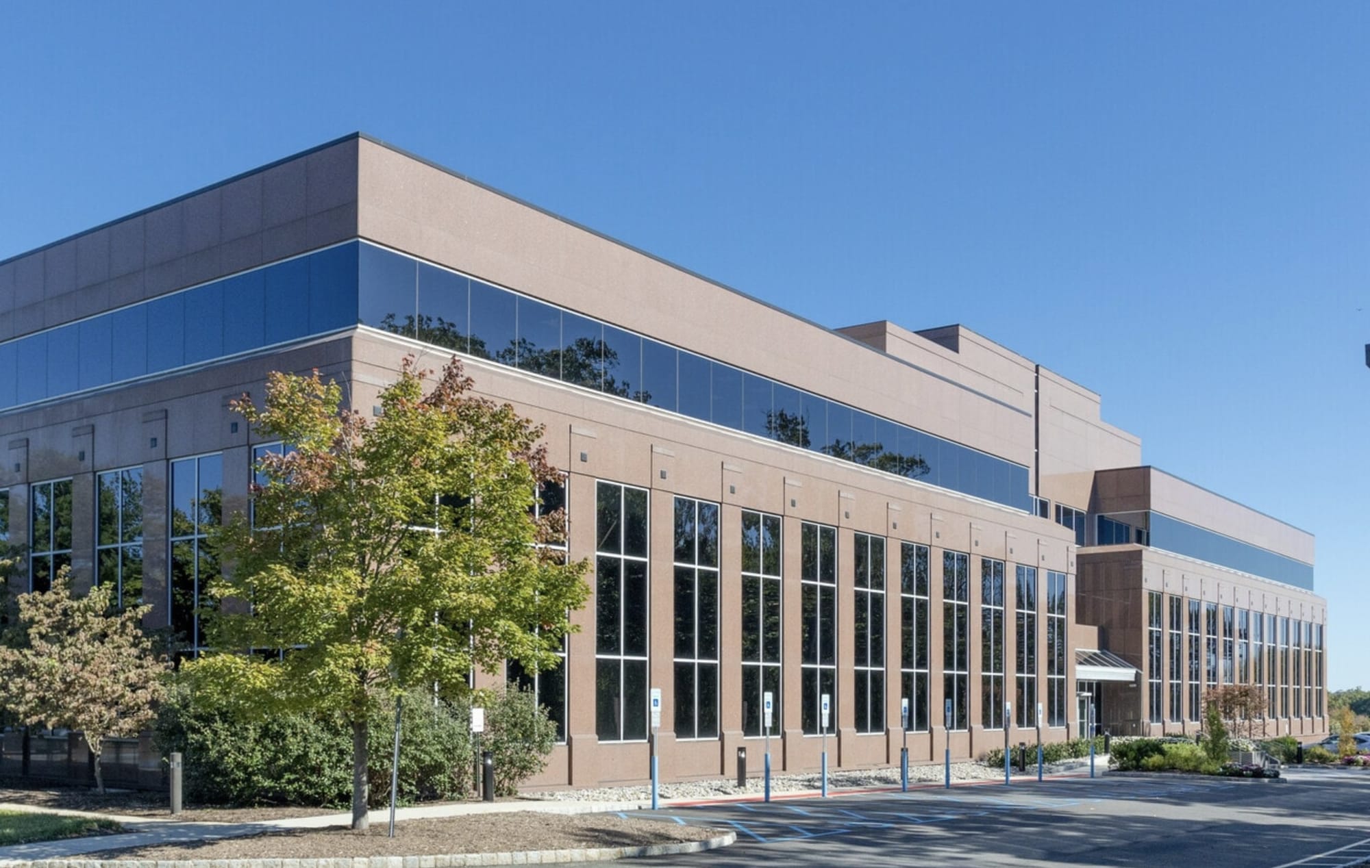 3 Mountainview Road in Warren Township, a three story office building with a rose granite facade and a blue glass band, the temporary home of the township offices, seen from the parking lot on a clear day.
