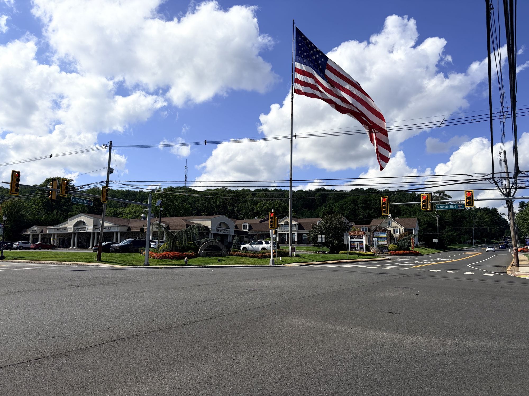 The Mt Bethel Road and Mountain Boulevard intersection in Warren Township, a large American flag flying over the shops at the town center, with street signs for both roads at the traffic signals.
