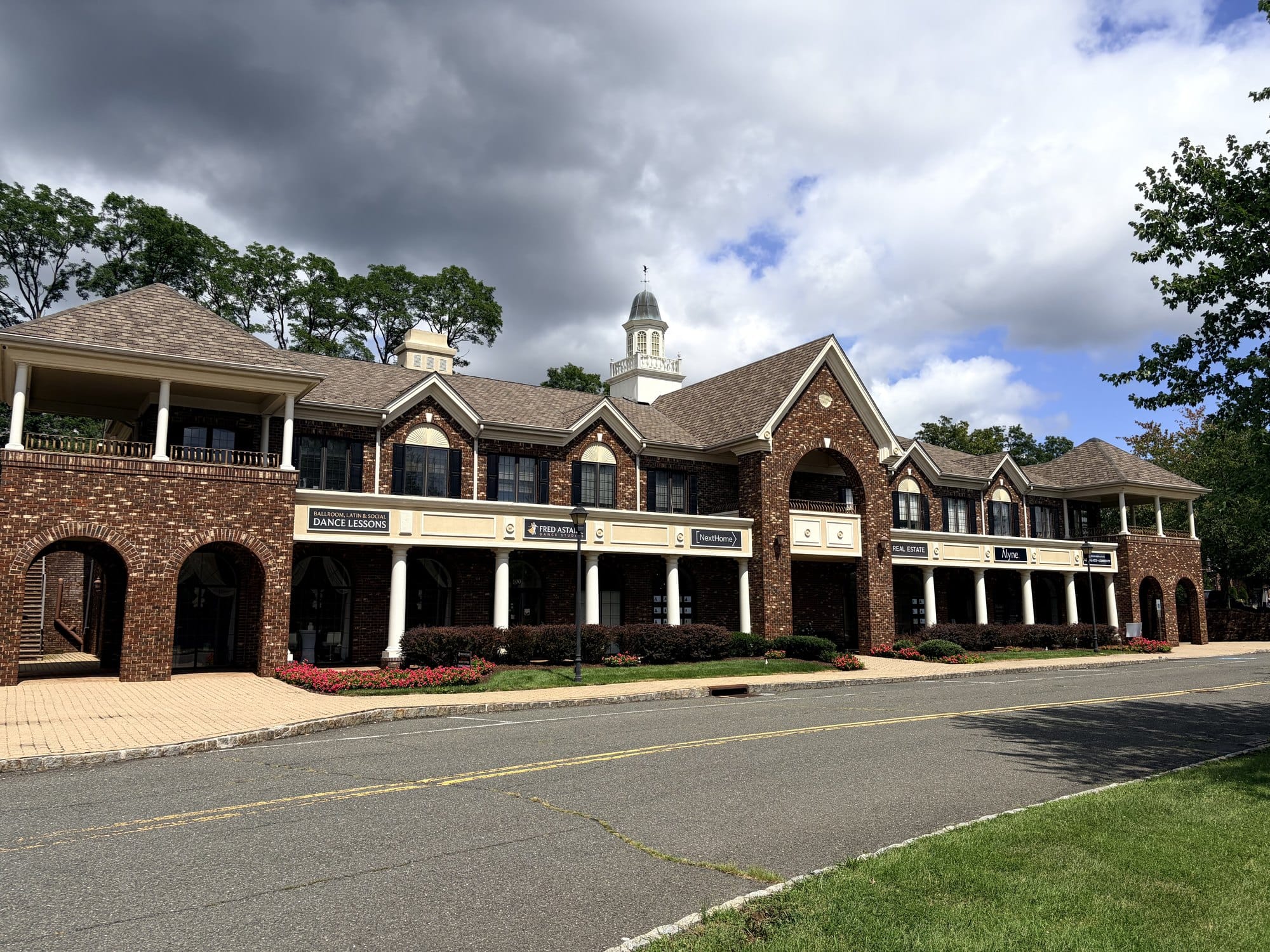The Town Center Drive office building in Warren Township, a brick building with a columned arcade and gabled dormers, tenant signs including NextHome and Real Estate along the front, and a white cupola above the roofline.