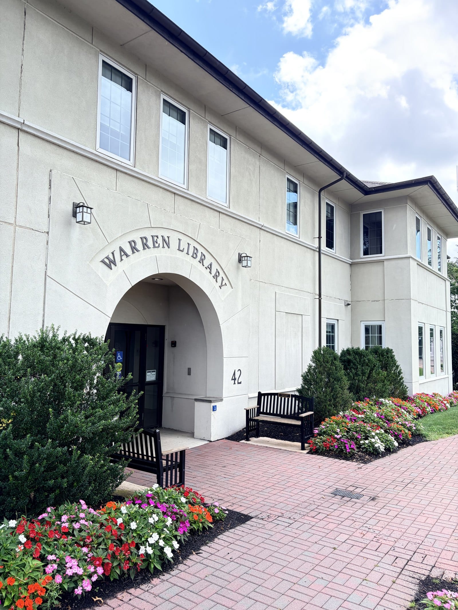 The Warren Library at 42 Mountain Boulevard, a cream building with WARREN LIBRARY carved in an arch over the entrance, the street number 42 beside it and benches and flower beds in front.