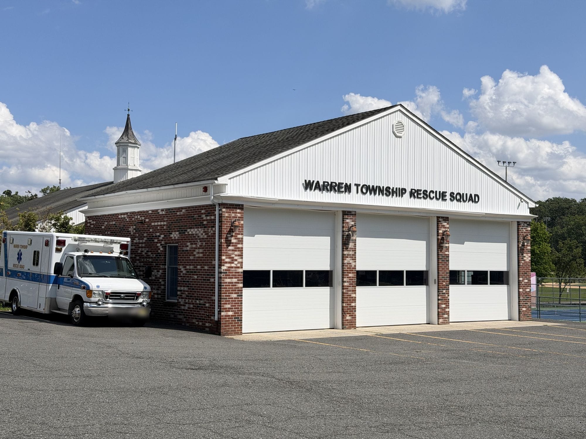 The Warren Township Rescue Squad building, a brick and white bay garage with three doors and WARREN TOWNSHIP RESCUE SQUAD lettered across the gable, an ambulance parked at the side.