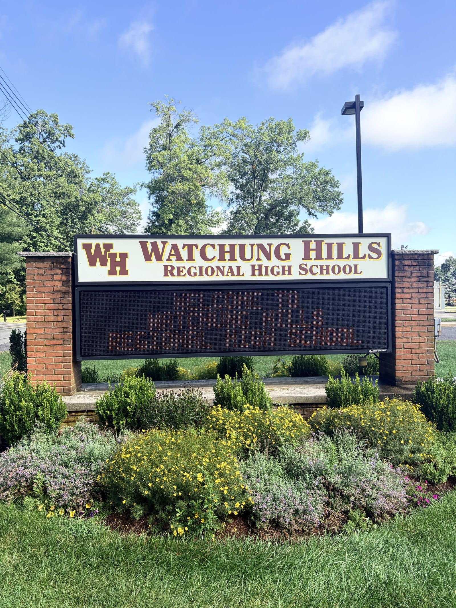 The Watchung Hills Regional High School sign on Stirling Road, a brick and white sign with the maroon WH monogram above an electronic message board reading Welcome to Watchung Hills Regional High School.