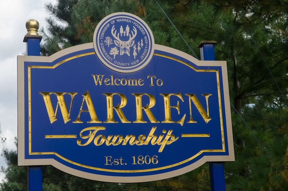 The Welcome To Warren Township sign, a blue and gold carved sign reading Welcome To Warren Township, Est. 1806, with the township seal mounted above it and pines behind.