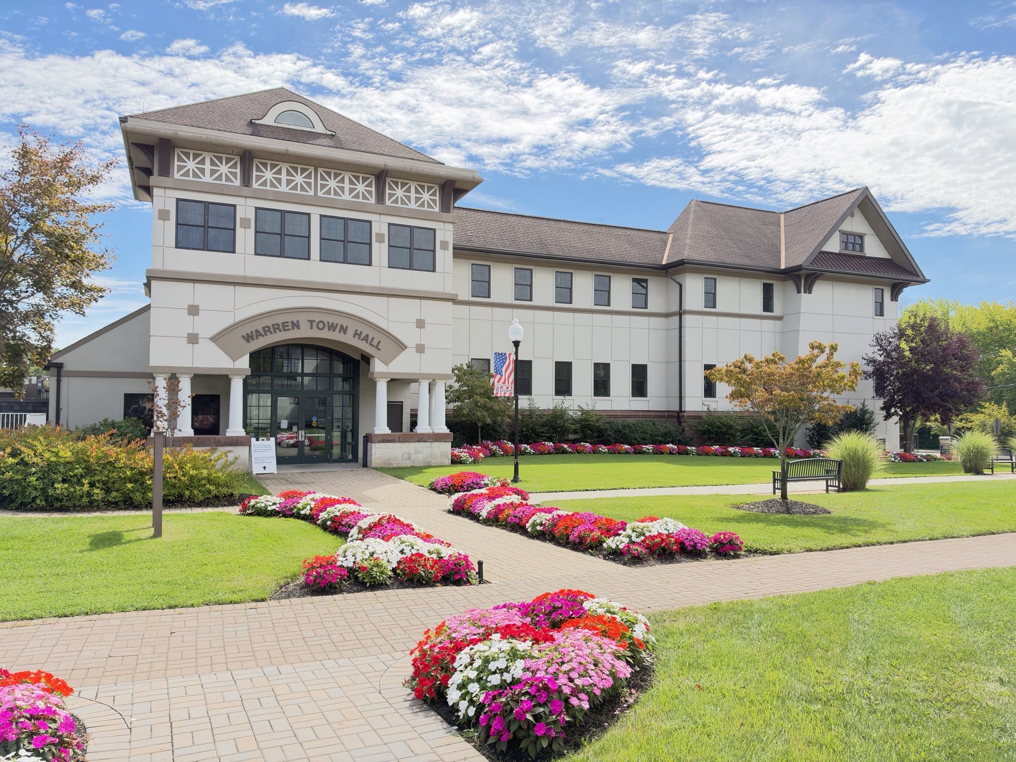 Warren Town Hall, a cream three story building with WARREN TOWN HALL over an arched glass entrance, behind brick walks and beds of red, pink and white impatiens.