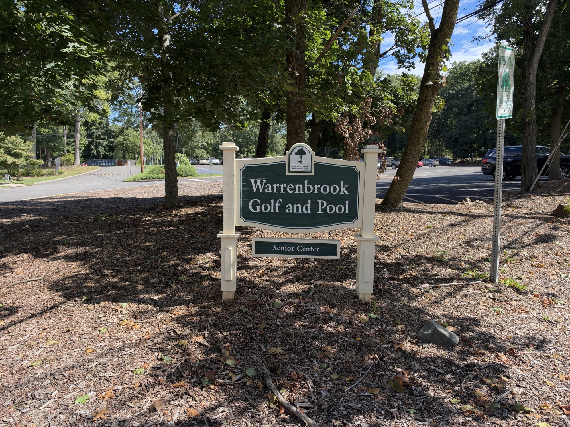 The Warrenbrook Golf and Pool sign with a Senior Center panel and the Somerset County Park Commission emblem, in a mulched bed by the parking lot.