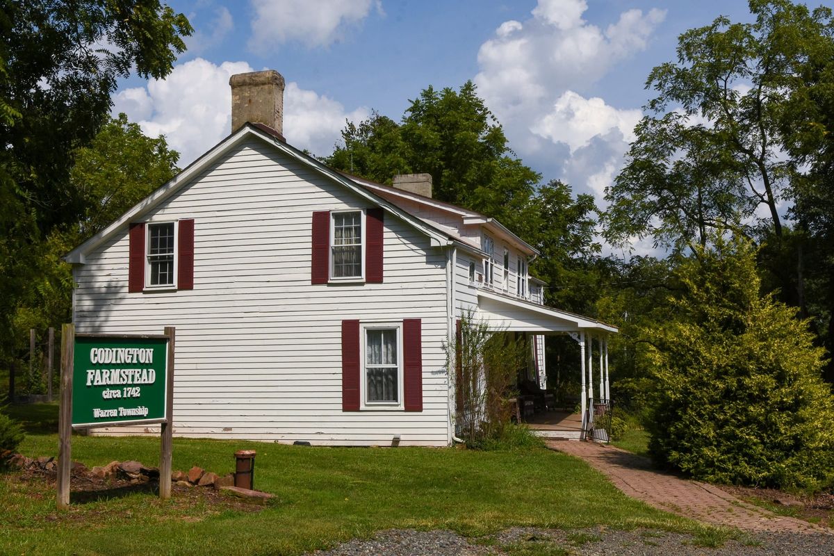 The Codington Farmstead in Warren Township, a white clapboard farmhouse with dark red shutters and a stone chimney, a green sign in front reading Codington Farmstead circa 1742.