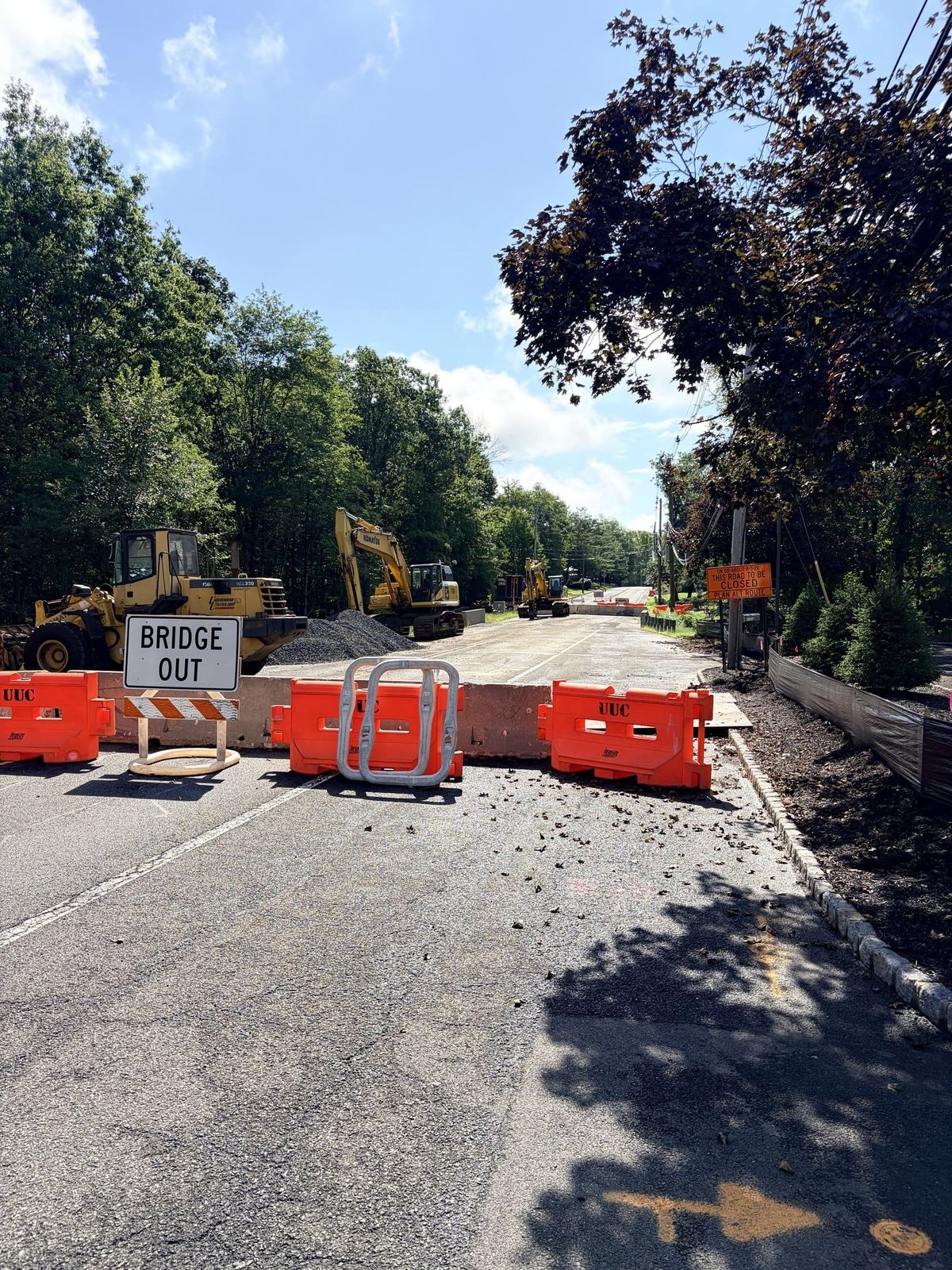 A Bridge Out sign and orange barriers closing Stirling Road in Warren Township, with excavators and a stockpile of stone on the closed roadway behind them.