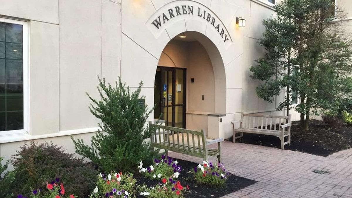 The arched stone entrance to the Warren Township Library at 42 Mountain Boulevard, with benches and flower beds by the door.