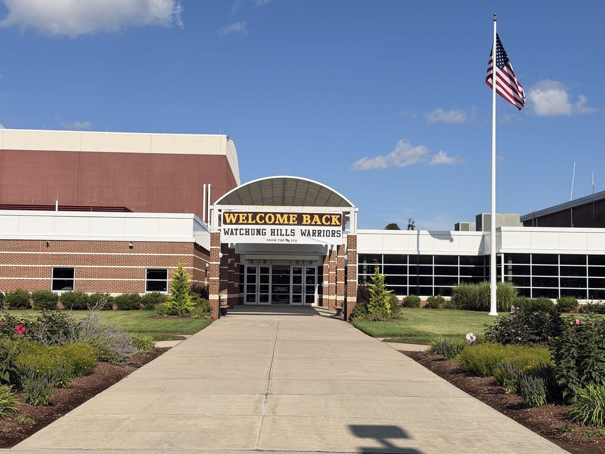 A WELCOME BACK WATCHUNG HILLS WARRIORS banner from the PTO hung under the arched entrance canopy at Watchung Hills Regional High School, with the flagpole and flag at right.