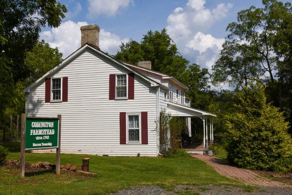 The Codington Farmstead in Warren Township, a white clapboard farmhouse with dark red shutters and a stone chimney, a green sign in front reading Codington Farmstead circa 1742.