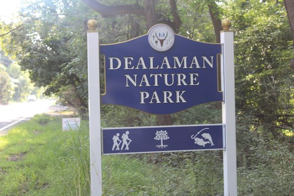 The Dealaman Nature Park entrance sign in Warren Township, a blue and gold sign with the township seal above it and a panel below showing hiking, tree and fishing symbols.