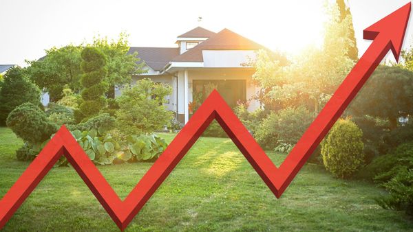 A suburban house at sunset behind a large red line chart arrow rising to the upper right, an illustration of housing market direction.