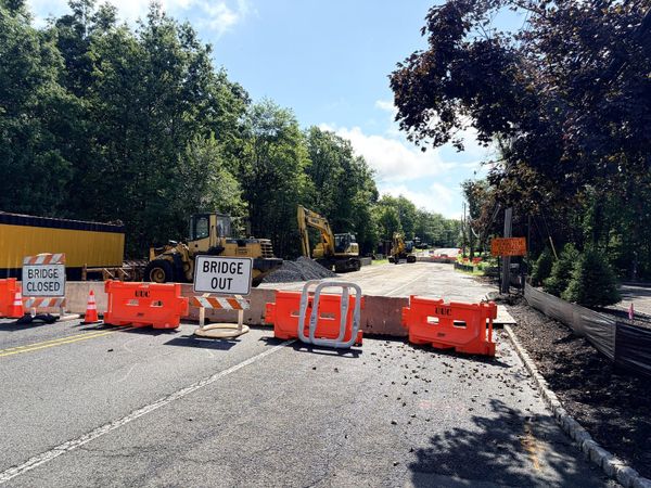 Stirling Road closed at the Stony Brook bridge in Warren Township, with Bridge Closed and Bridge Out signs, orange barriers across both lanes and excavators at the removed deck beyond.