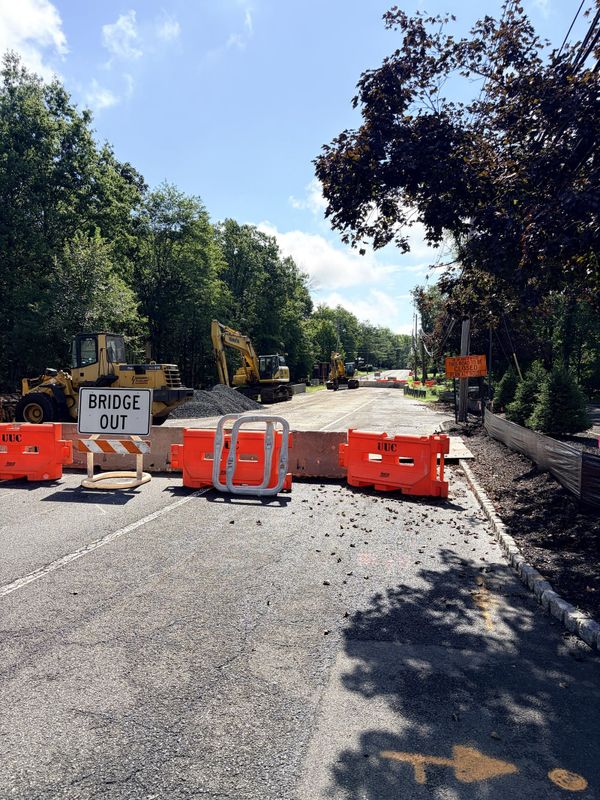 A Bridge Out sign and orange barriers closing Stirling Road in Warren Township, with excavators and a stockpile of stone on the closed roadway behind them.