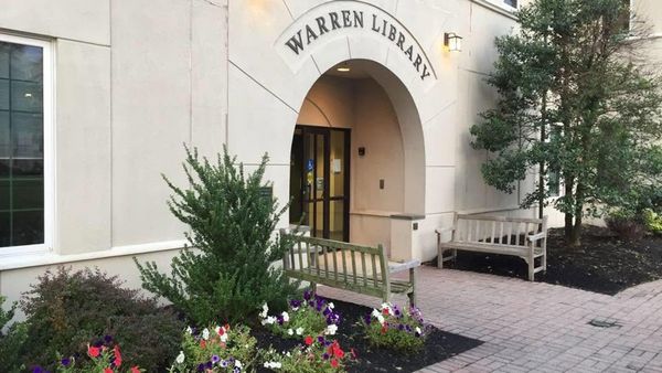 The arched stone entrance to the Warren Township Library at 42 Mountain Boulevard, with benches and flower beds by the door.