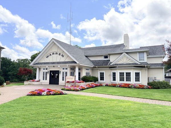 The Warren municipal building that houses the municipal court, meeting room and police department, a cream building with WARREN lettered on the front gable and flower beds along the walk.