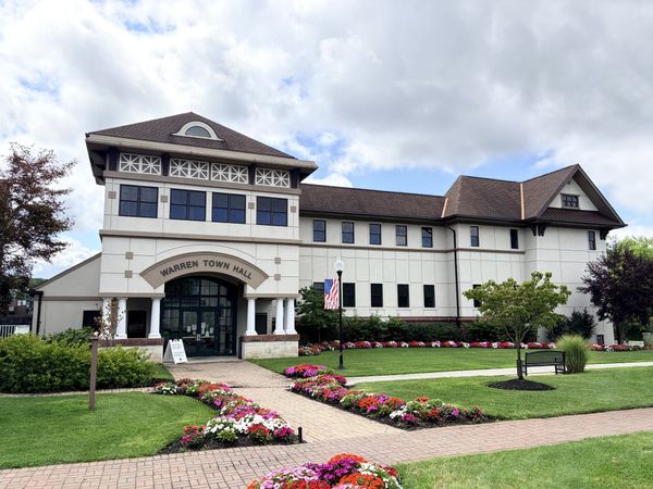 Warren Town Hall, a cream stucco and brick municipal building with WARREN TOWN HALL lettered over a columned entrance, flower beds and a brick walk leading to the door.