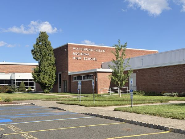 Watchung Hills Regional High School, a brick building with WATCHUNG HILLS REGIONAL HIGH SCHOOL lettered across the upper wall above the entrance walk and reserved parking signs.