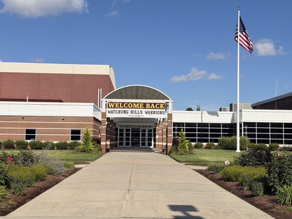 A WELCOME BACK WATCHUNG HILLS WARRIORS banner from the PTO hung under the arched entrance canopy at Watchung Hills Regional High School, with the flagpole and flag at right.