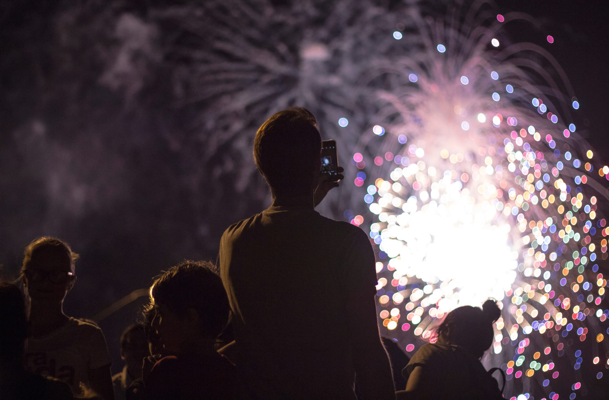 A man taking a picture of the fireworks in Tokyo during a summer festival at night