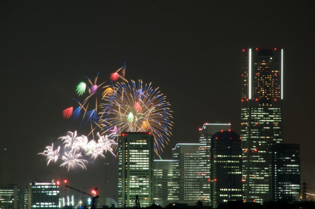 Fireworks in Tokyo during a summer festival at night, behind some tall buildings