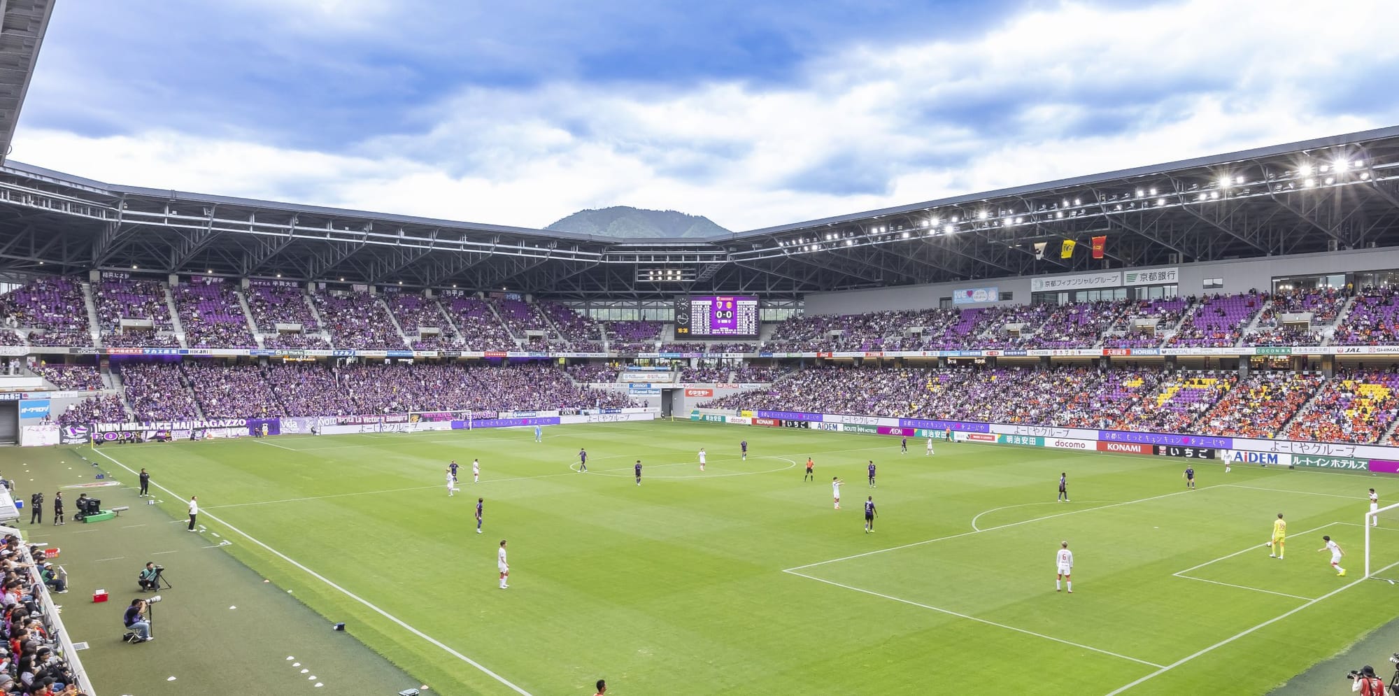 Sanga Stadium with purple seats hosts a soccer match, teams in white and purple.