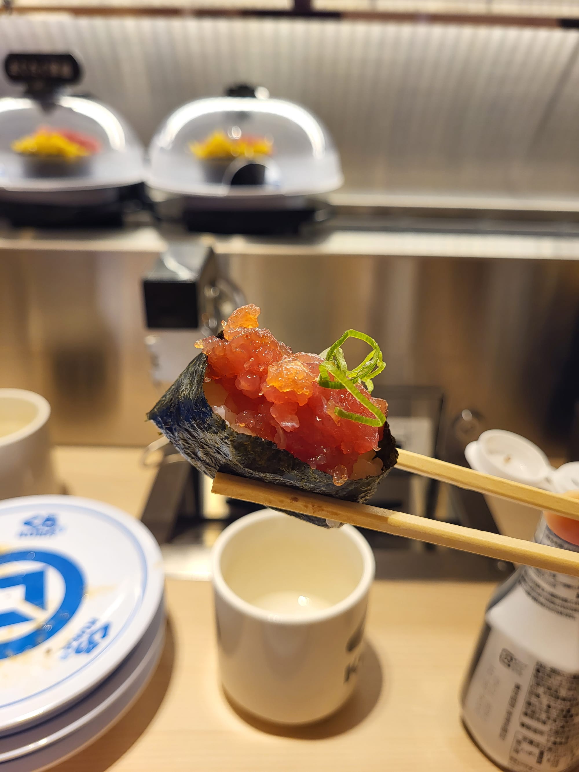 a woman holding a piece of sushi with chopsticks at a conveyor belt restaurant in Tokyo, Japan