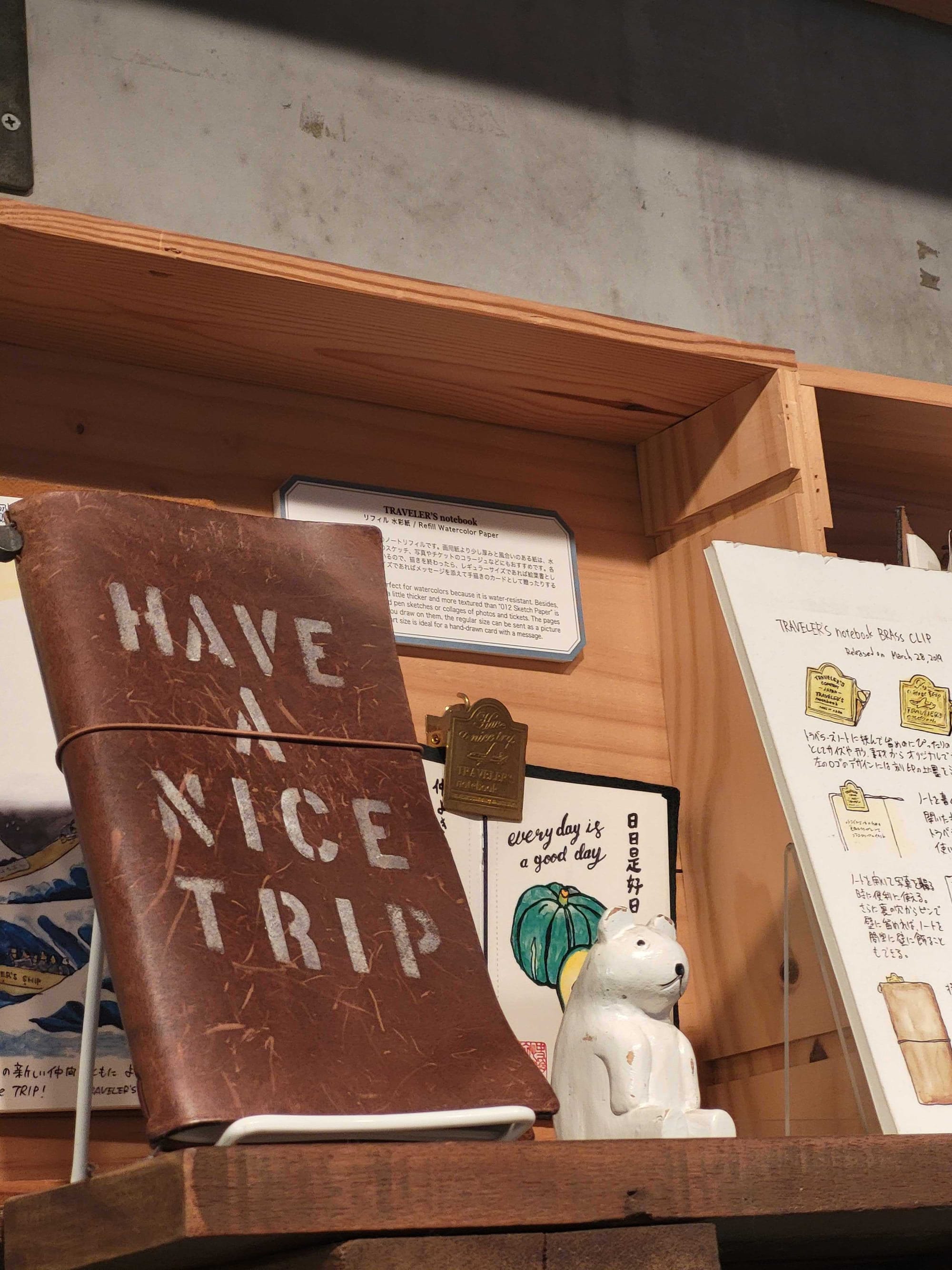 A leather journal with the words "Have a nice trip" stamped on it, sitting on a shelf next to a wooden polar bear.
