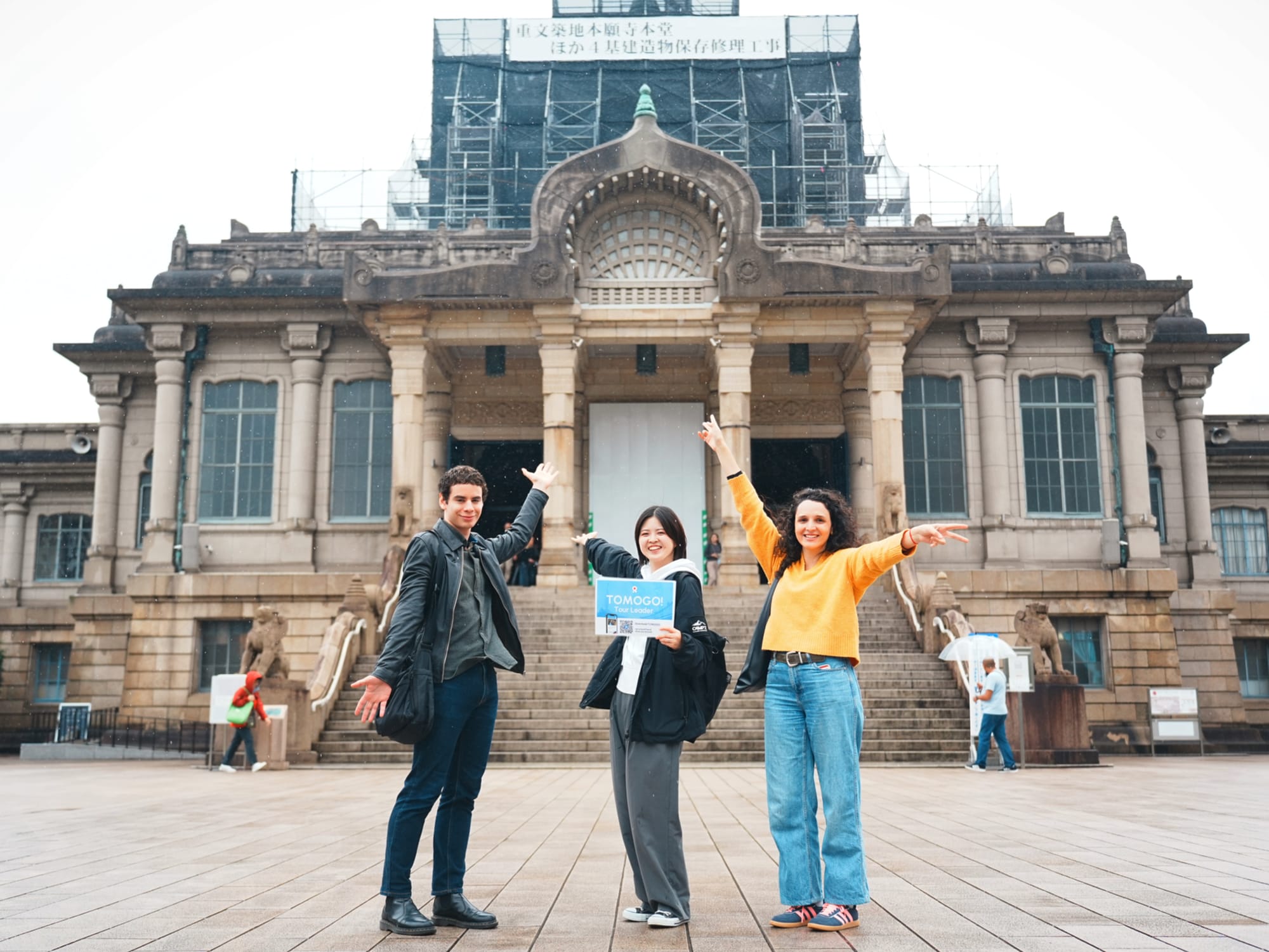 Three people pose with arms raised,  in front of Tsukiji Honganji.