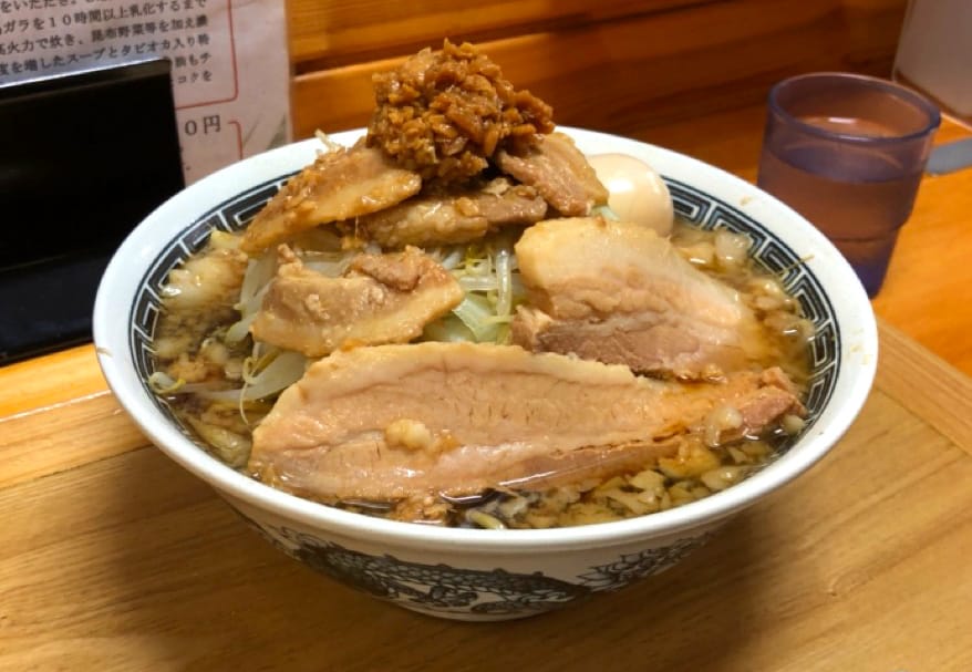 A big bowl of ramen with many pieces of meat, at the counter of a ramen restaurant