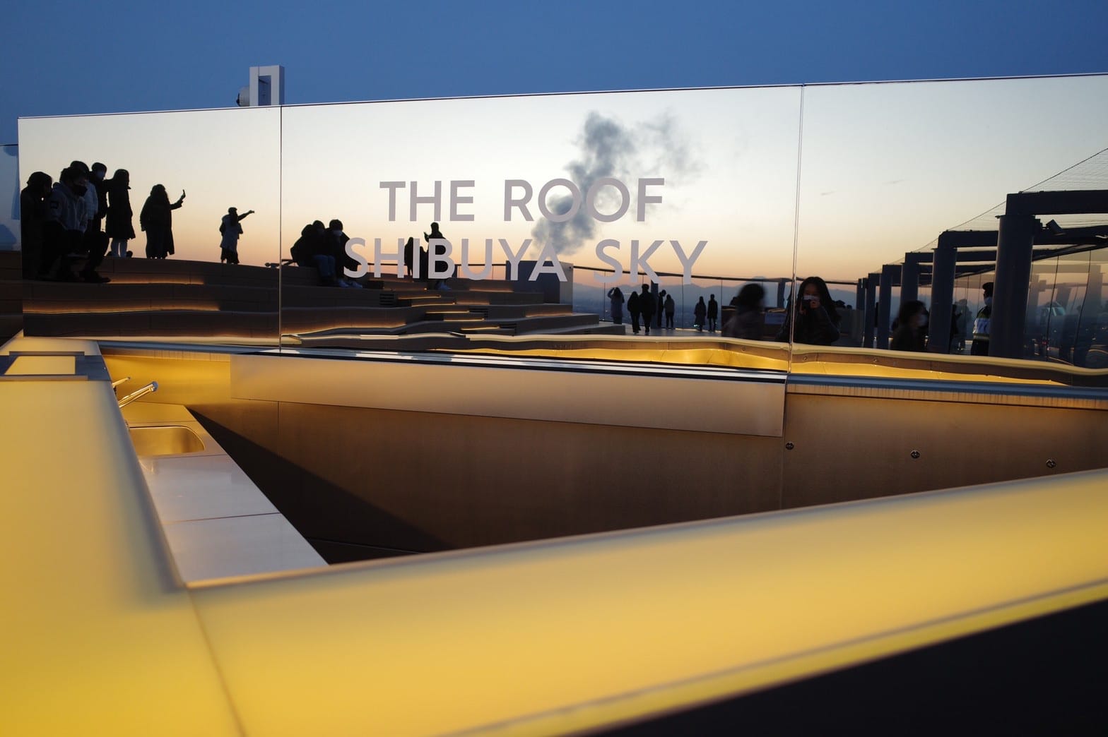 People silhouetted against a sunset gather at THE ROOF SHIBUYA SKY.