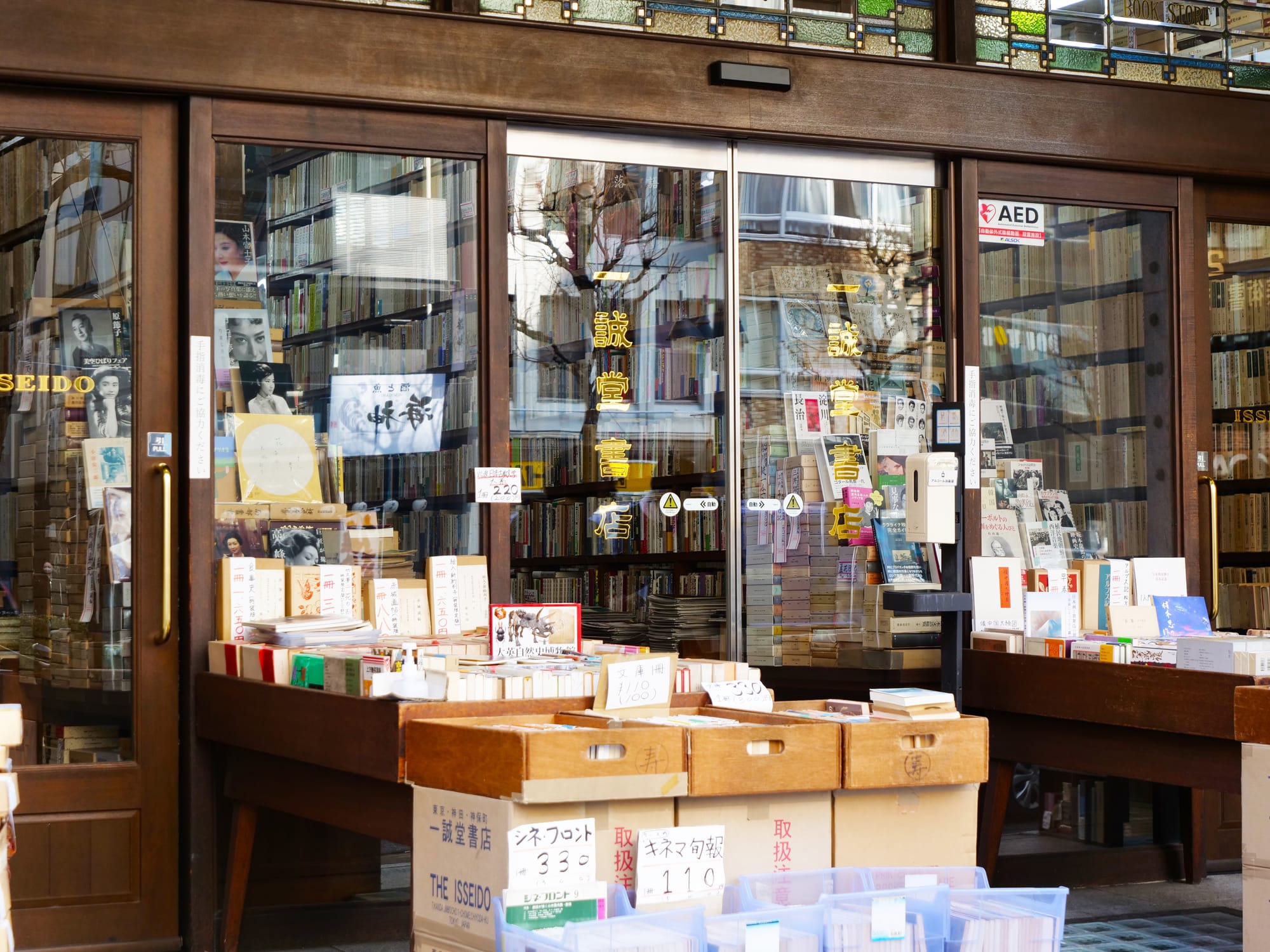 Bookstore entrance in Jimbocho with wooden doors and large windows displaying stacked books.