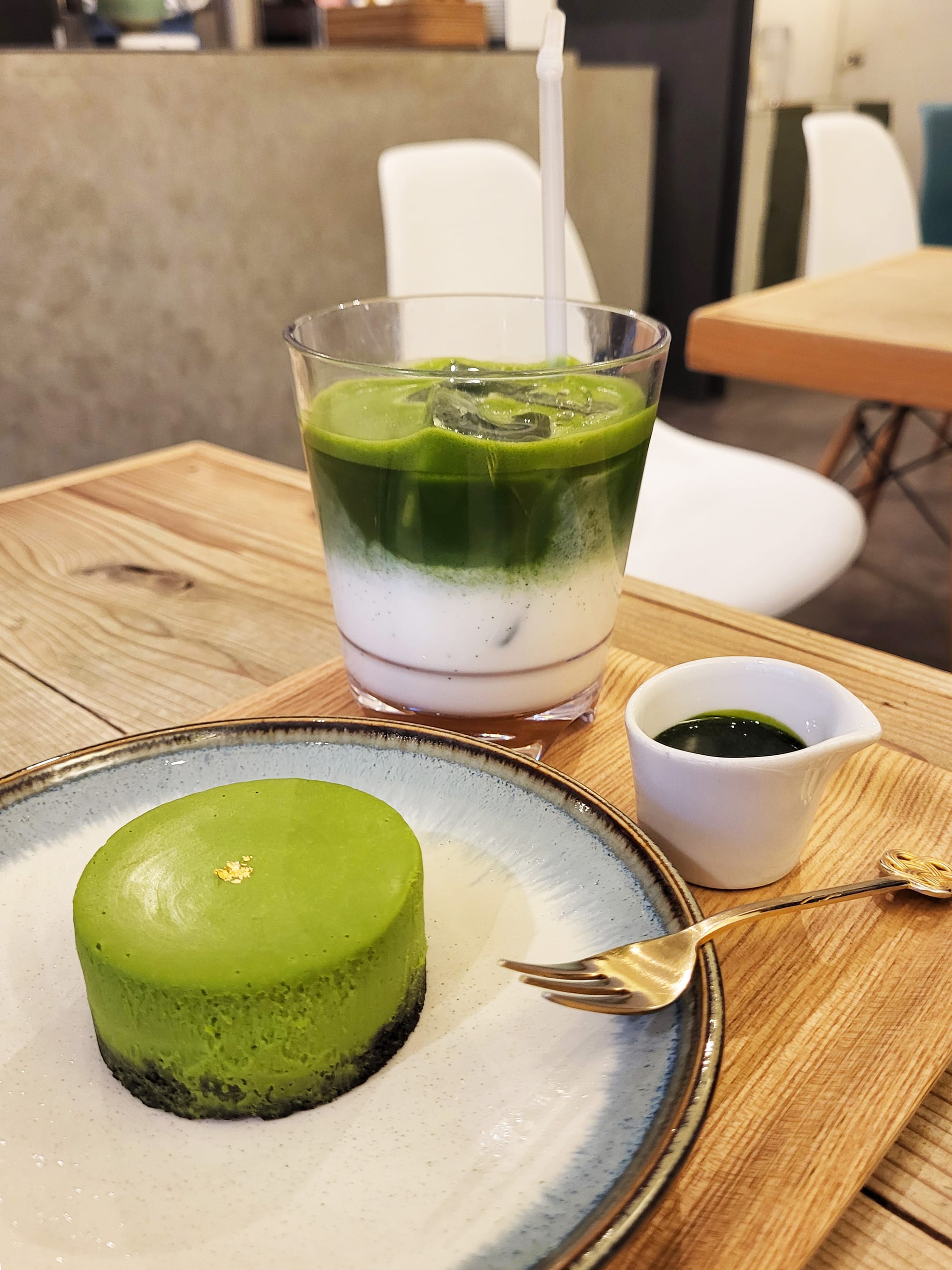 Matcha cake with gold leaf, iced matcha latte, and sauce on a wooden table.