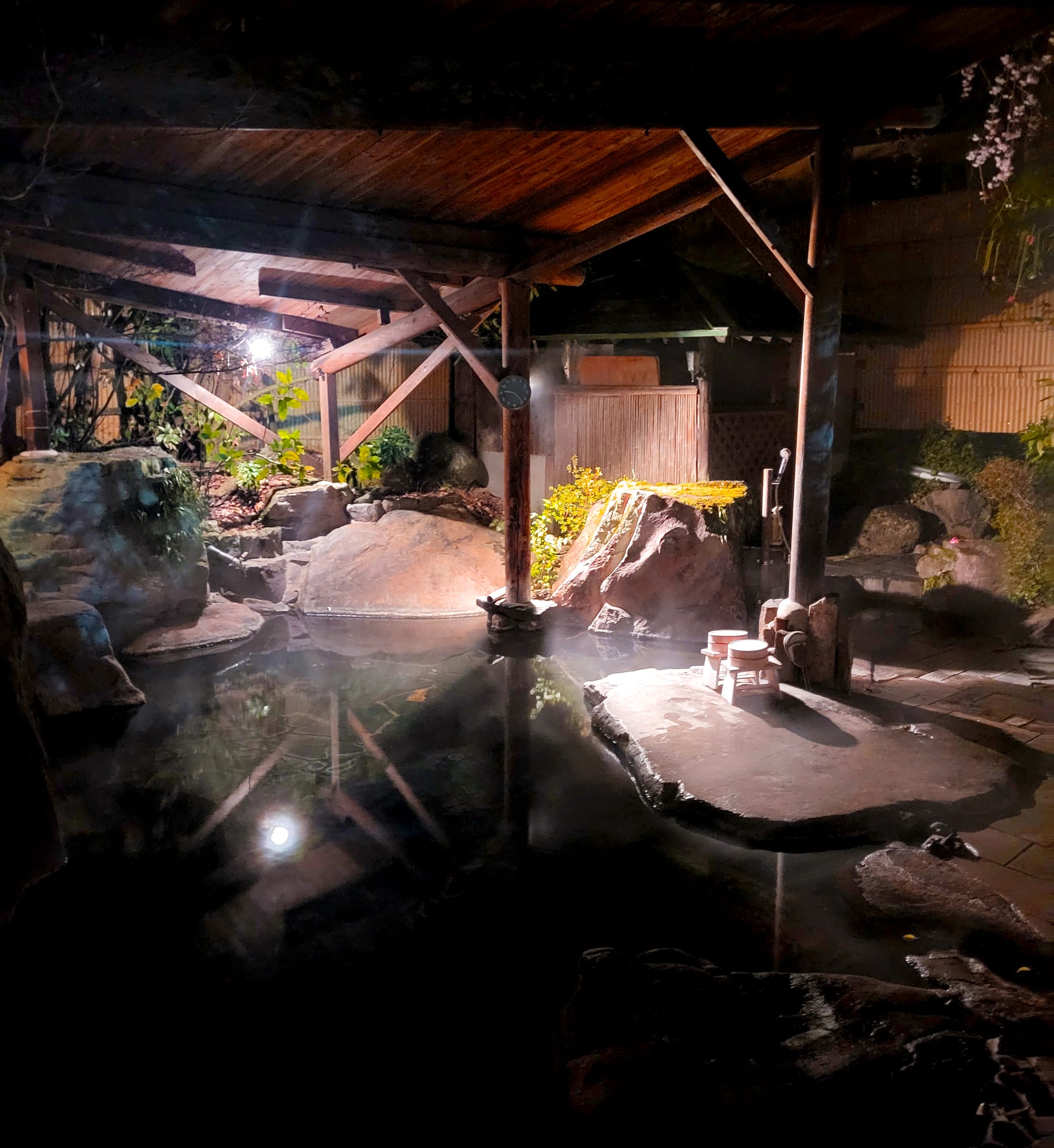 Tranquil hot spring at night with rock formations and wooden beams.