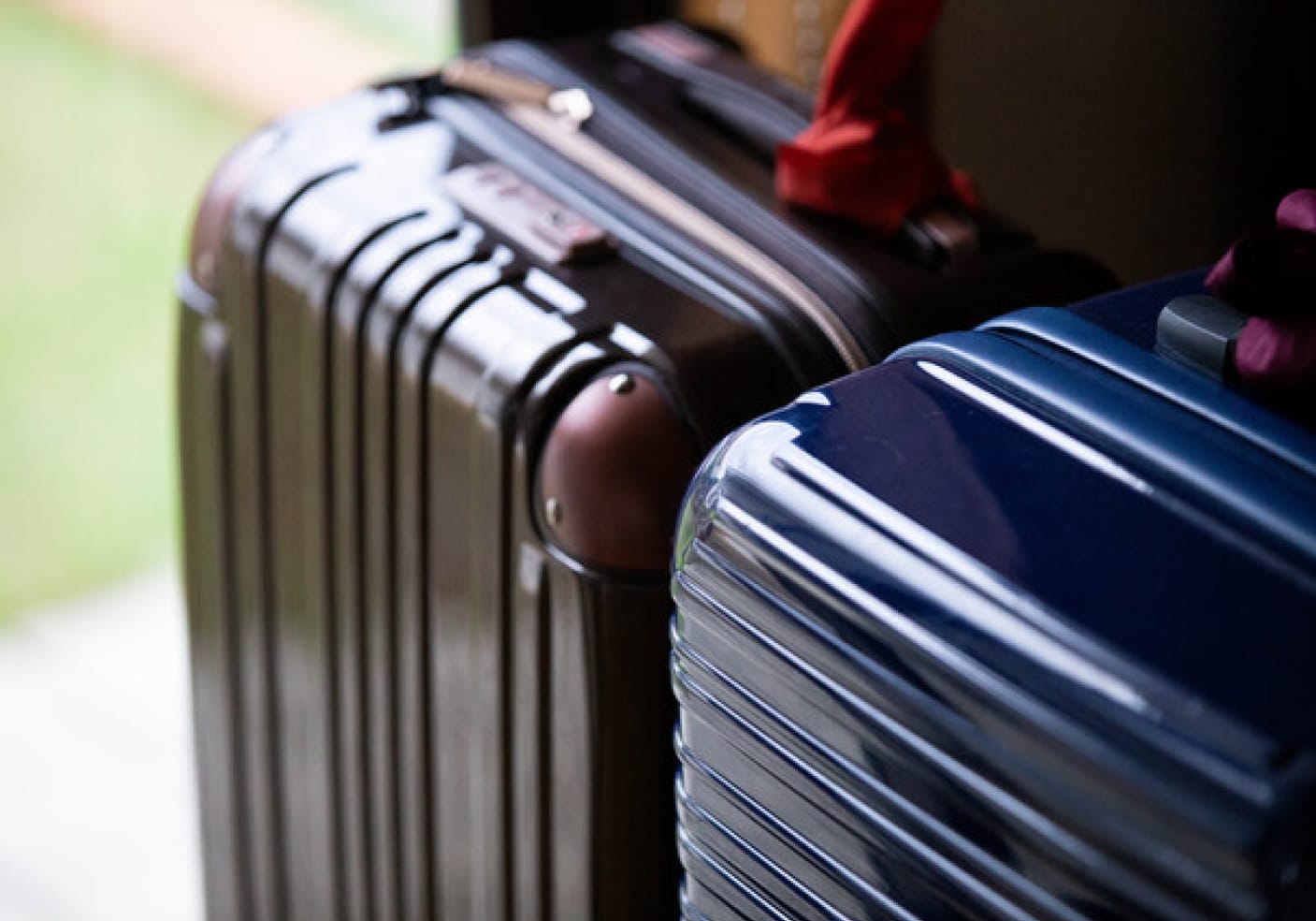 Two hard-shell suitcases, one brown and one blue, with red and purple scarves tied to handles. Soft natural light in a blurred background.