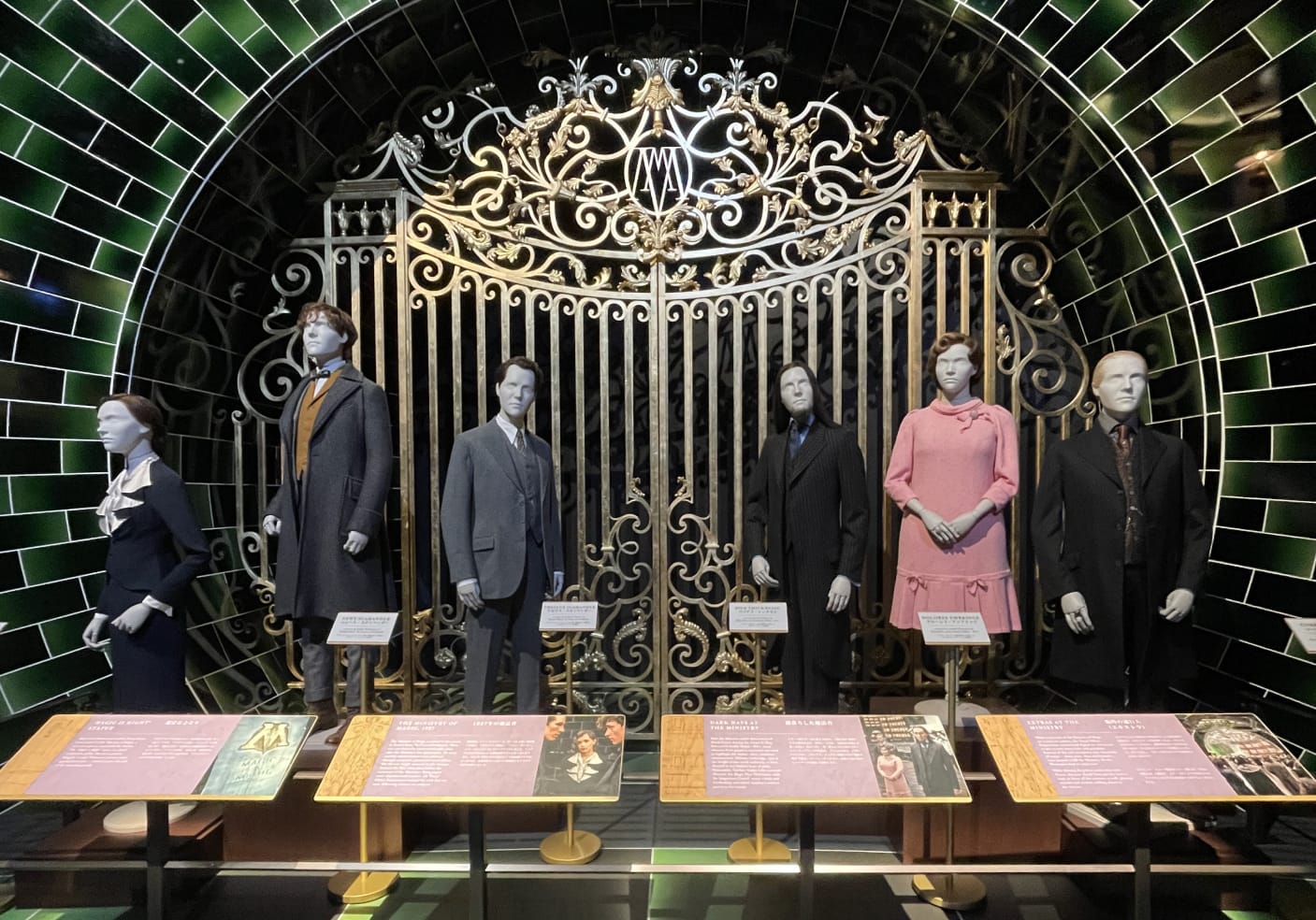 Movie characters mannequins in costumes lined up in front of an ornate gate with green-tiled walls. Informative signs on stands display text.