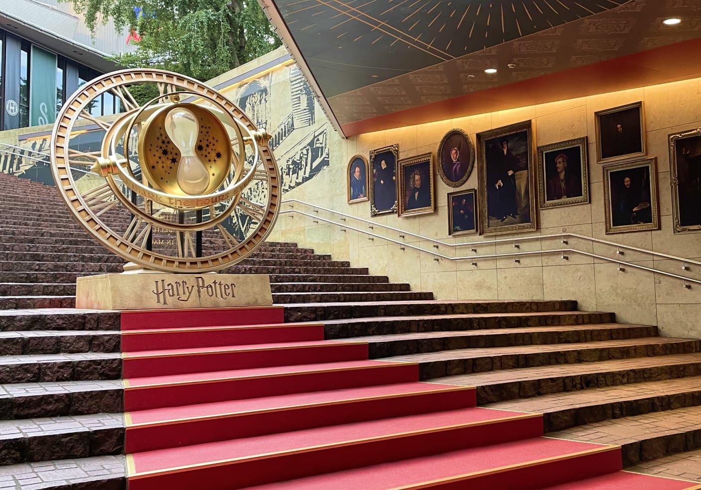 Golden time-turner on red-carpeted stairs with framed portraits on the wall. 
