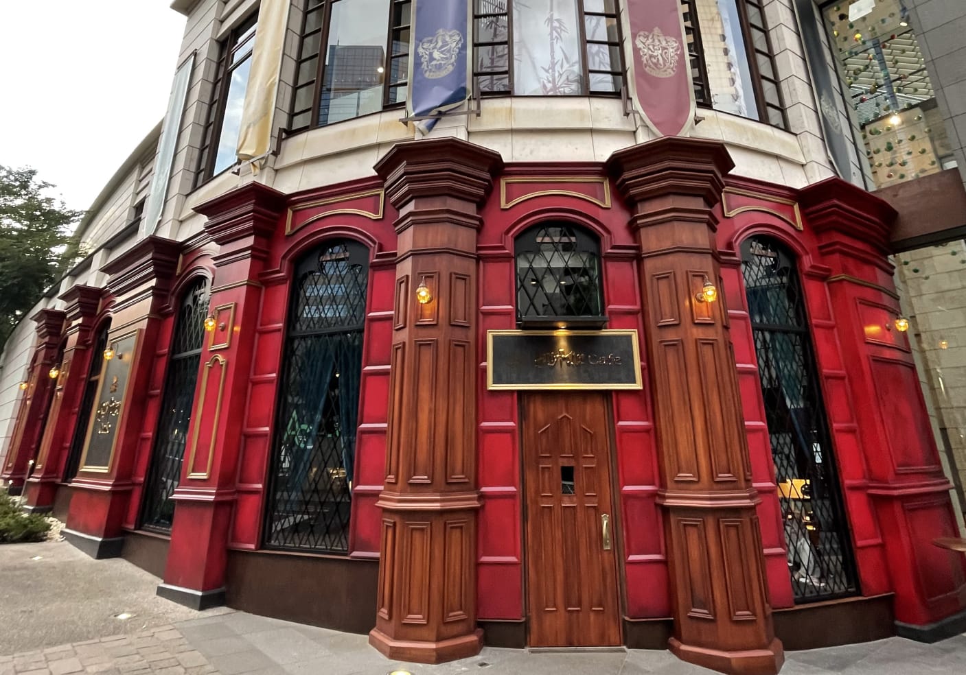 Red and wood facade of Harry Potter Cafe with ornate windows, lanterns, and banners above. 