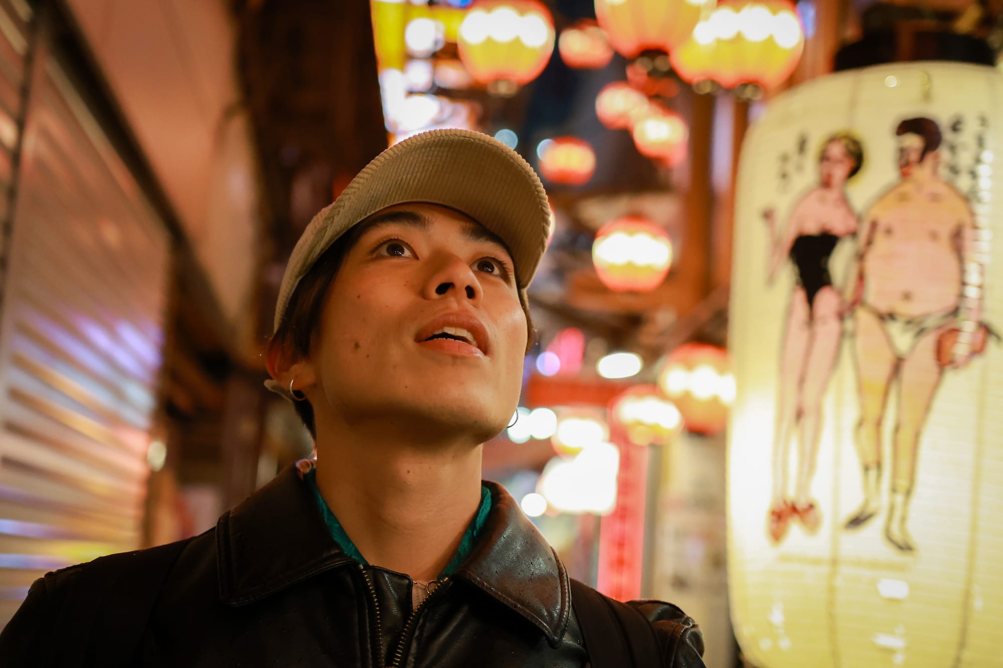 A young Japanese man looking at the lights on a busy street in Tokyo at night.