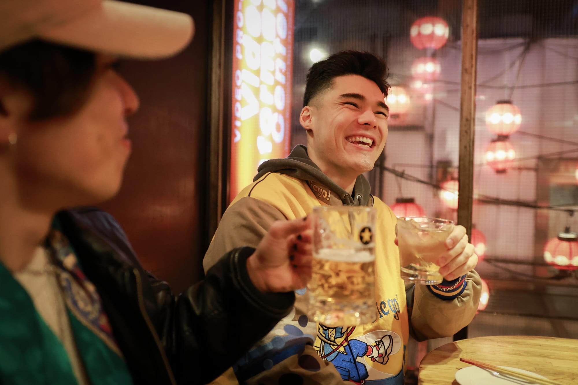 2 Japanese friends laughing and holding some beer glasses at a bar in Tokyo.