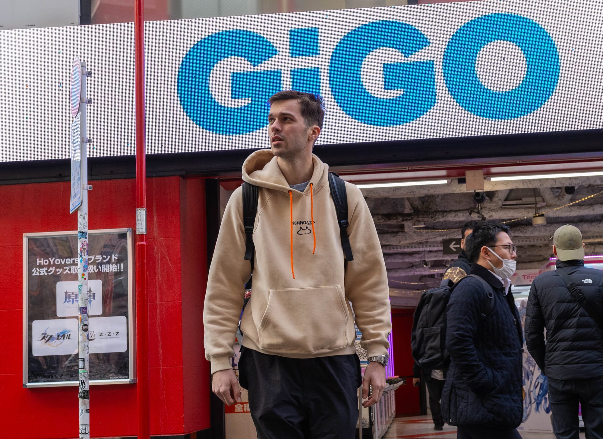 A man standing in front of an arcade in Tokyo, Japan, with a big neon sign that says GiGO