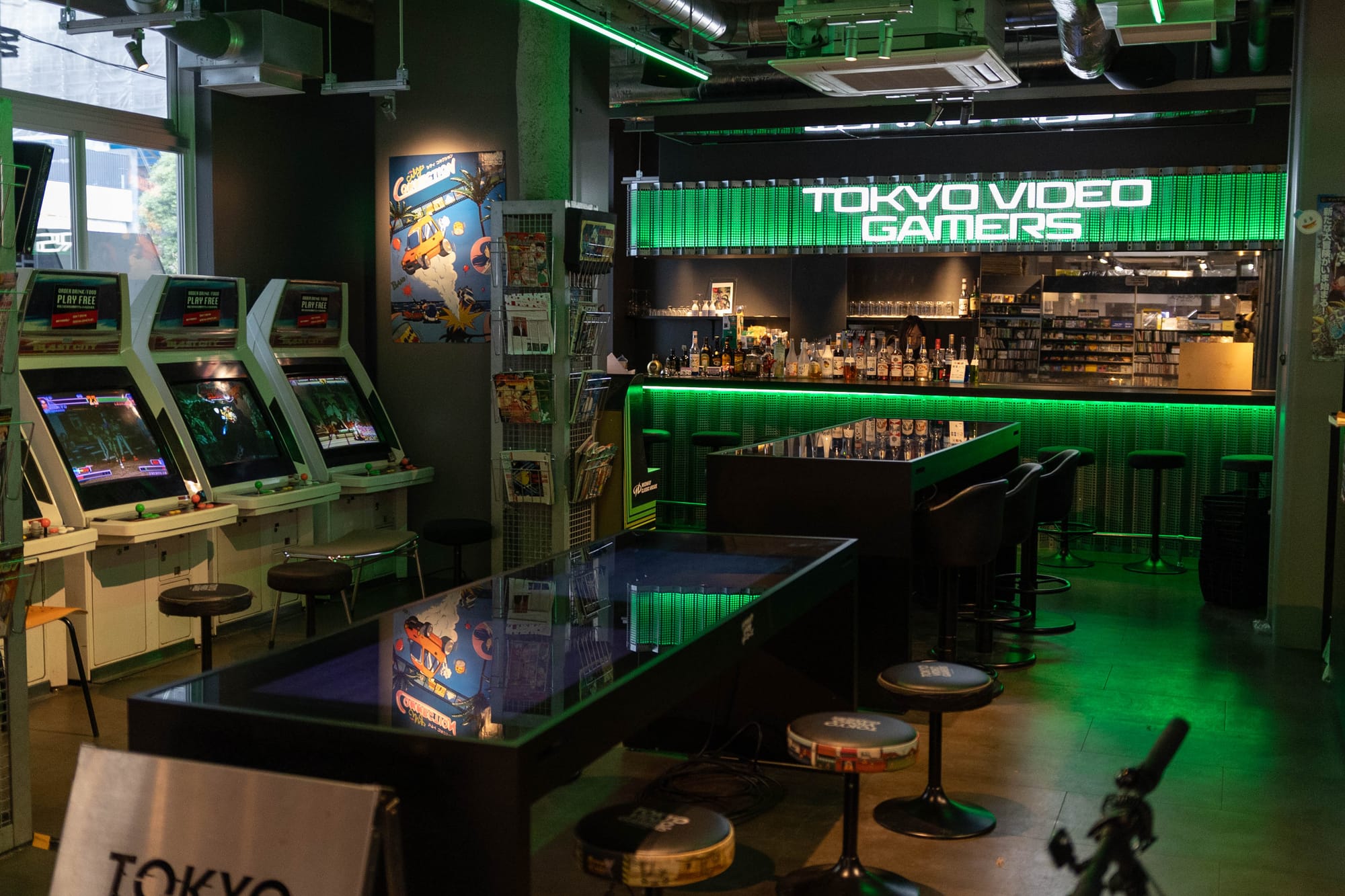 A picture of the inside of a retro video game bar in Tokyo, Japan, with green neon lights and tables.