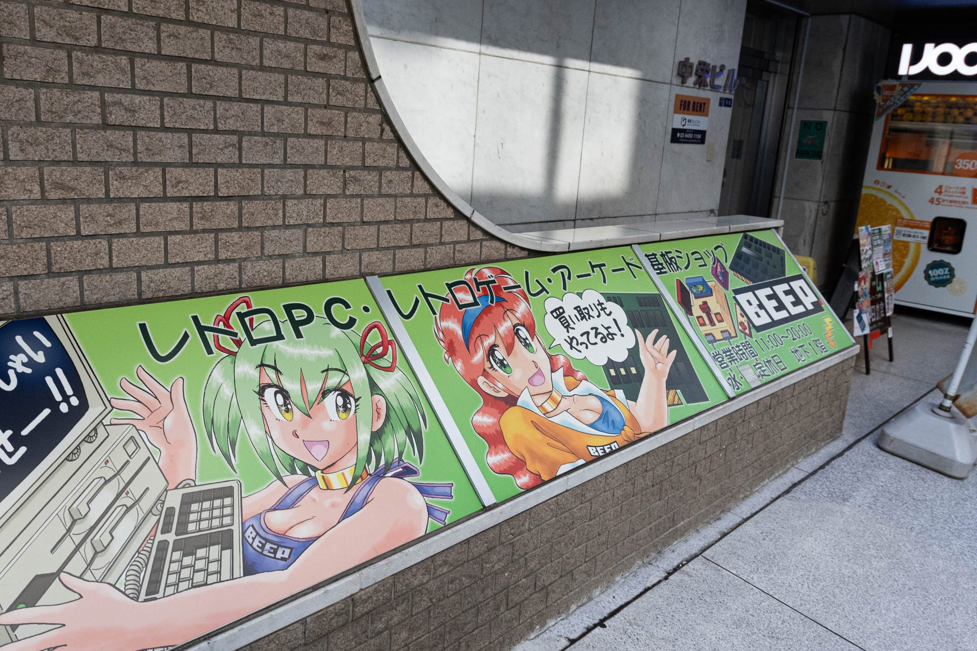 A picture of a green sign outside a retro game shop, with anime pictures and games