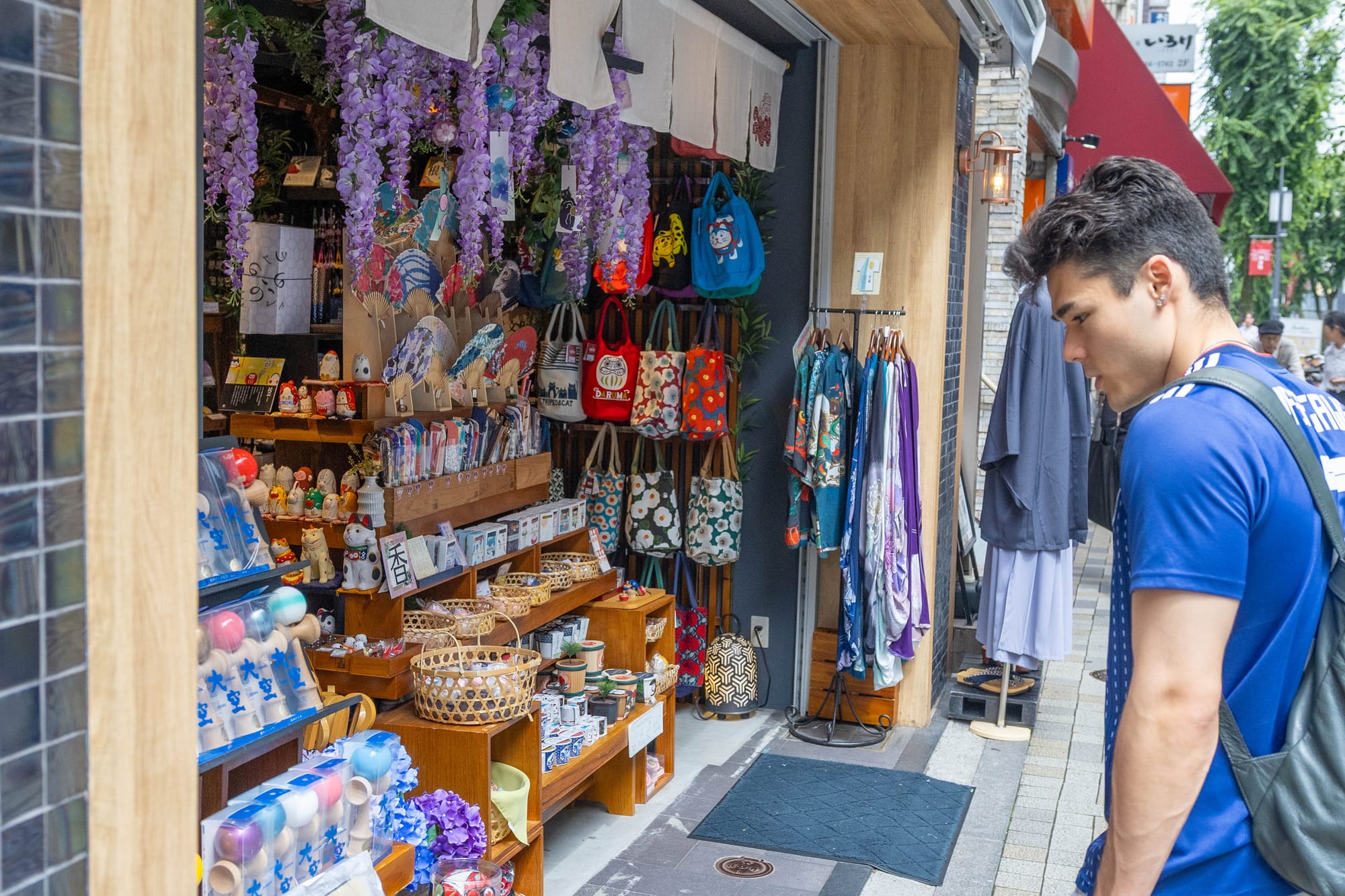 Man browsing a Japanese market stall with bags, fans, and decor.