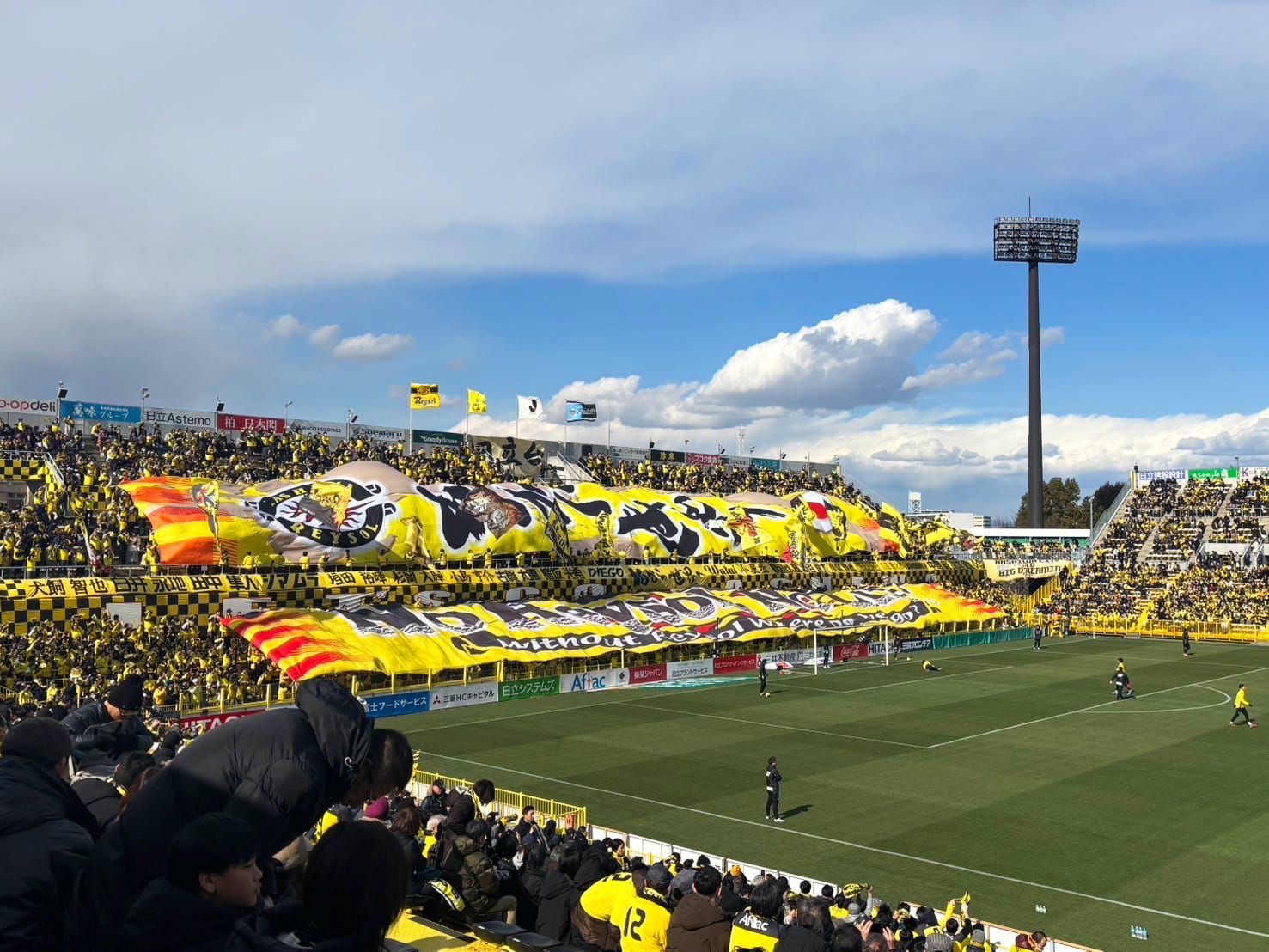 Kashiwa Reysol soccer game with cheering crowd waving large yellow banners.