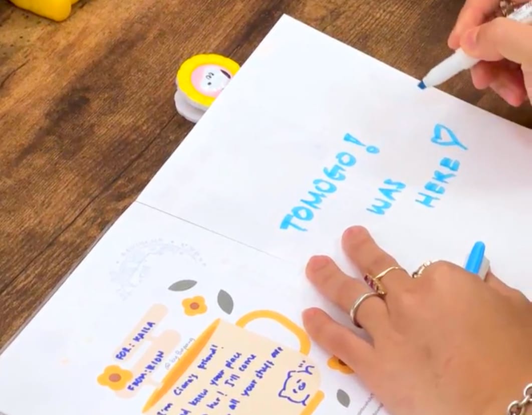 A picture of the front page of a notebook and a person writing a message on it with a blue pen at a stationery store in Tokyo