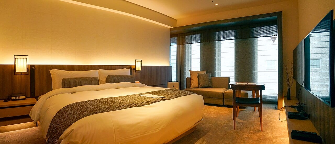 The Thousand Hotel room in Kyoto with a large bed, soft lighting, and a modern sofa. 